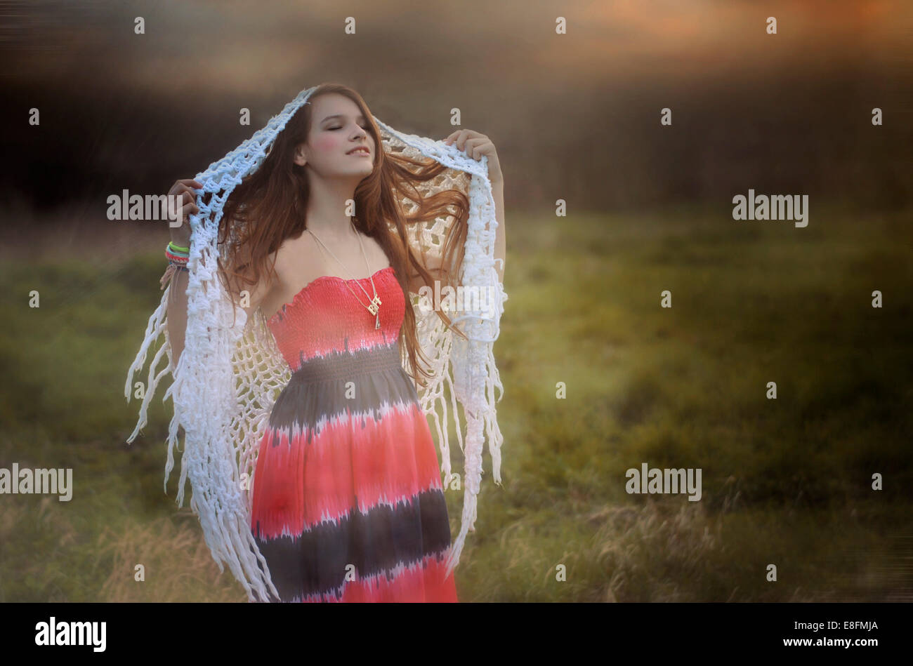 Teenage girl standing in a meadow holding a shawl on her head, Poland Stock Photo