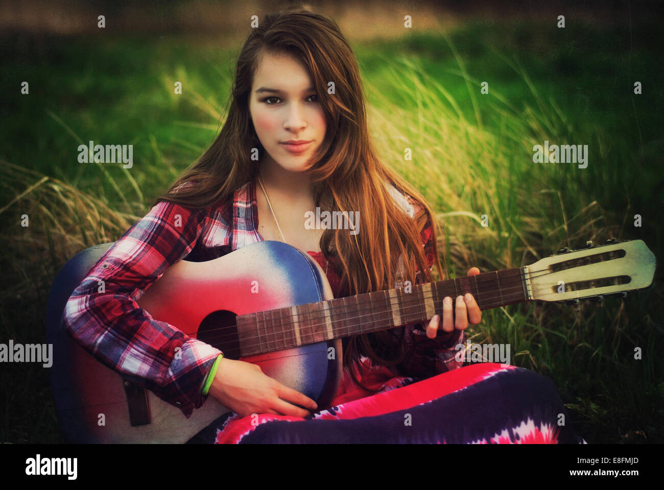 Portrait of a teenage girl sitting in a meadow with her guitar, Poland Stock Photo