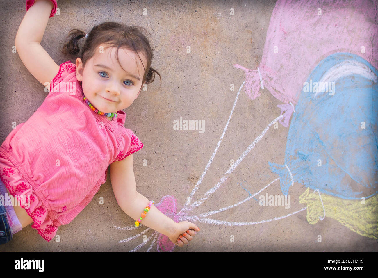Texas, United States of America Little Girl Laying On Ground With Chalk Drawn Balloons Stock Photo