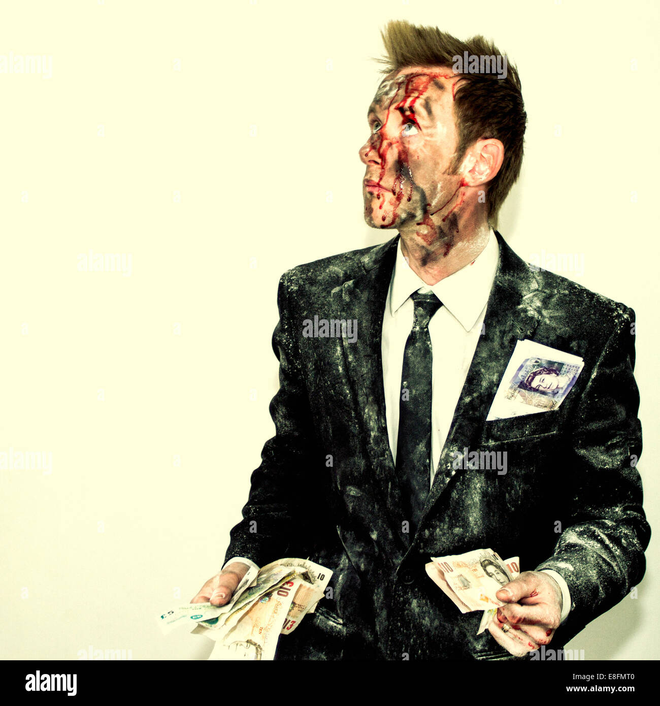 Bloodied man in a dirty suit holding a handful of money Stock Photo