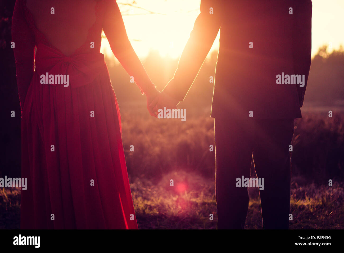 Couple standing in a meadow holding hands at sunset Stock Photo