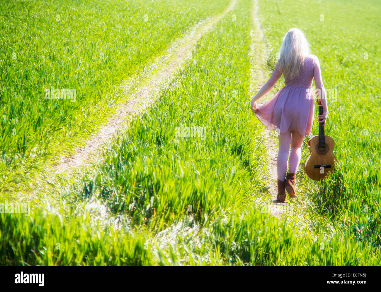 Rear view of young woman walking on green field with guitar Stock Photo