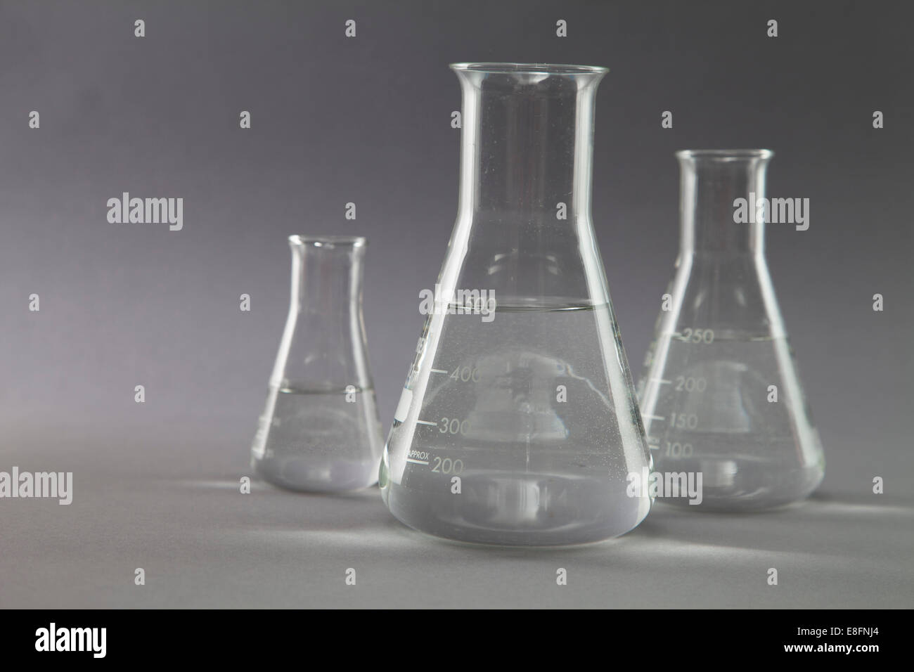 Three conical flasks and measuring beakers filled with clear liquid in
