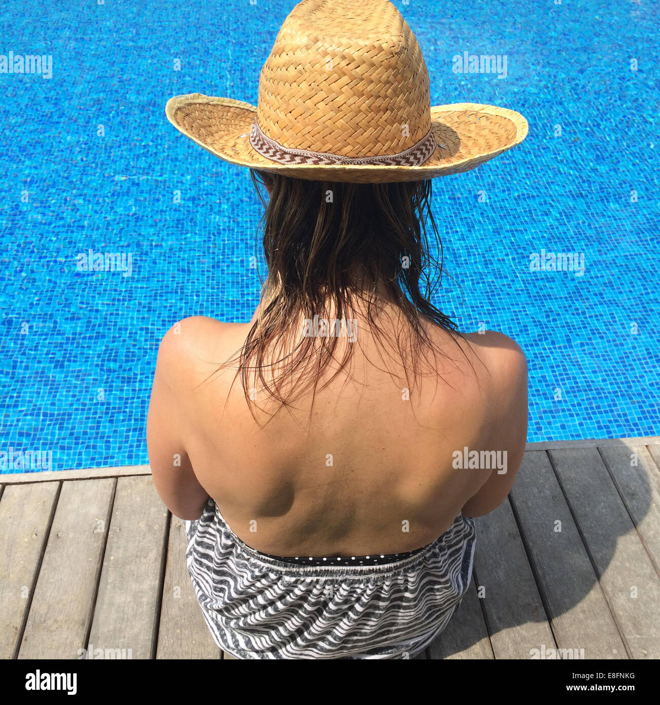 Rear view of woman sitting at the edge of a swimming pool Stock Photo