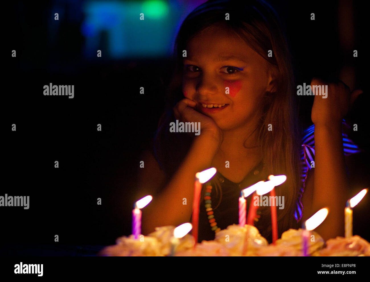 Smiling girl with heart shaped face paint sitting by her birthday cake Stock Photo