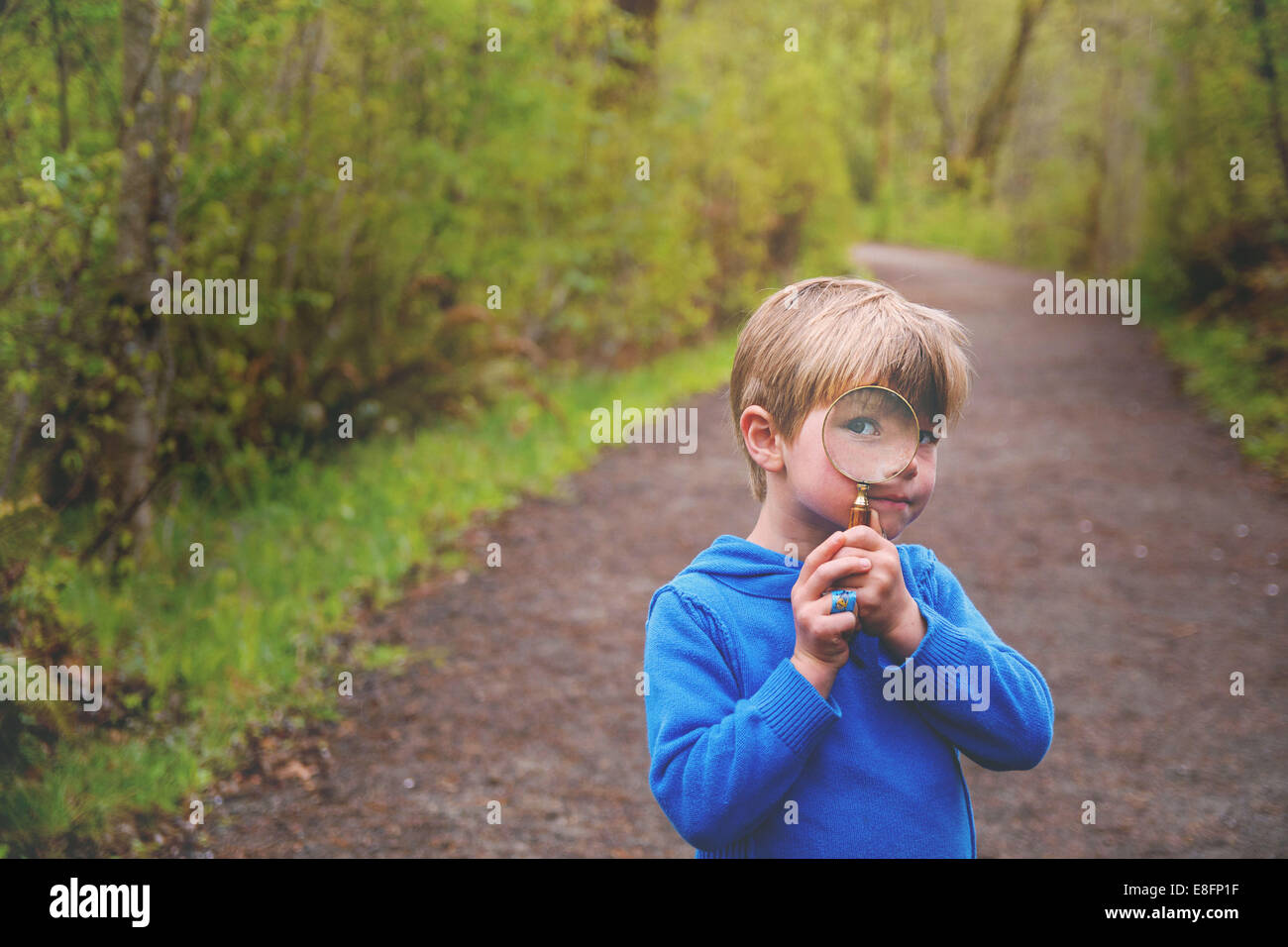 Boy standing a footpath looking through magnifying glass , USA Stock Photo