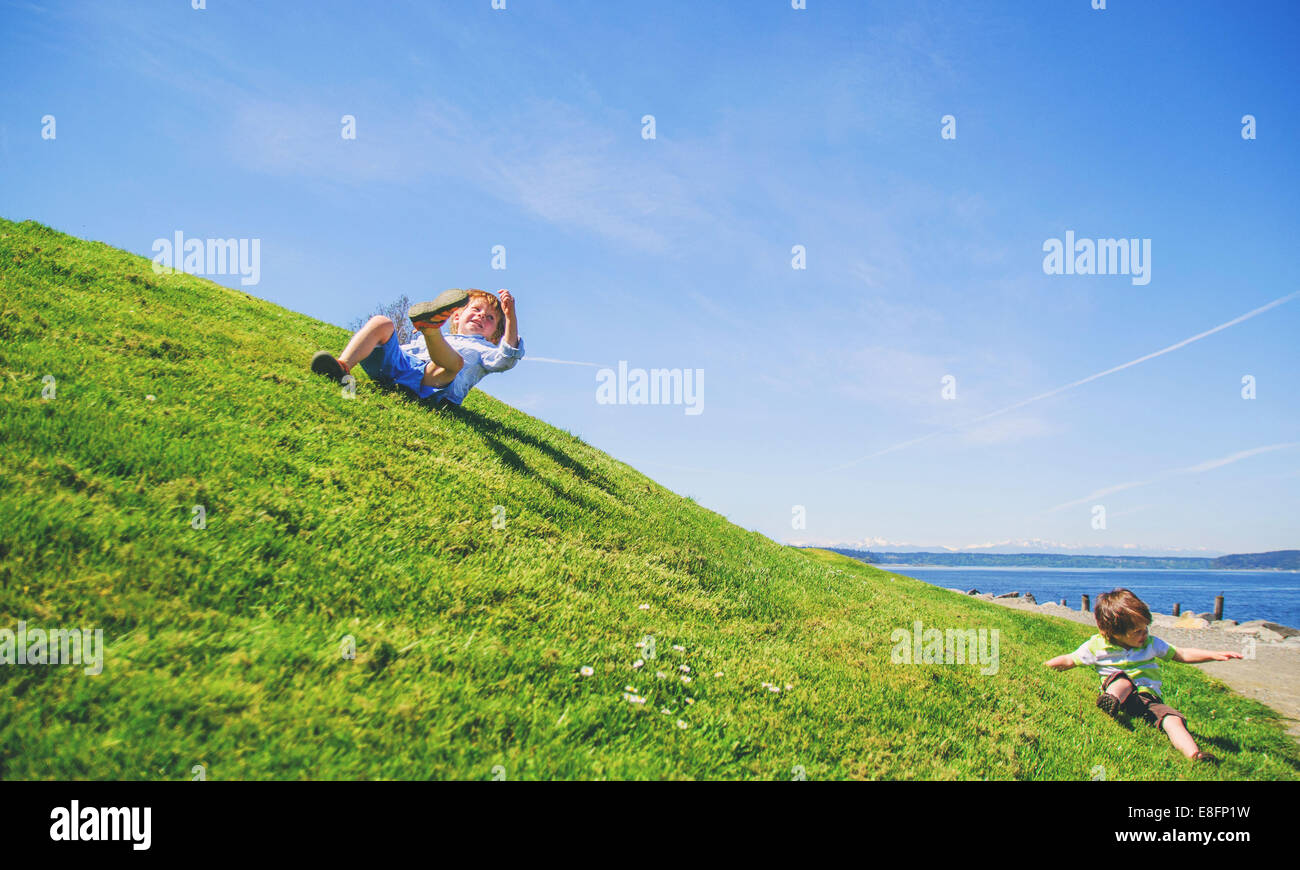 Two boys rolling down grassy hill, USA Stock Photo