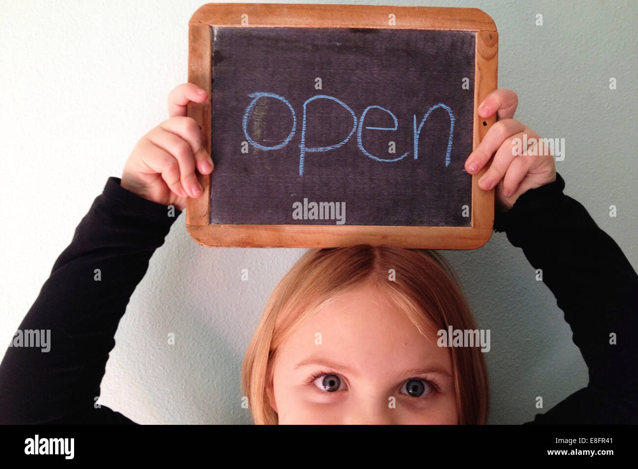 Portrait of a girl holding a blackboard above her head with the word open Stock Photo