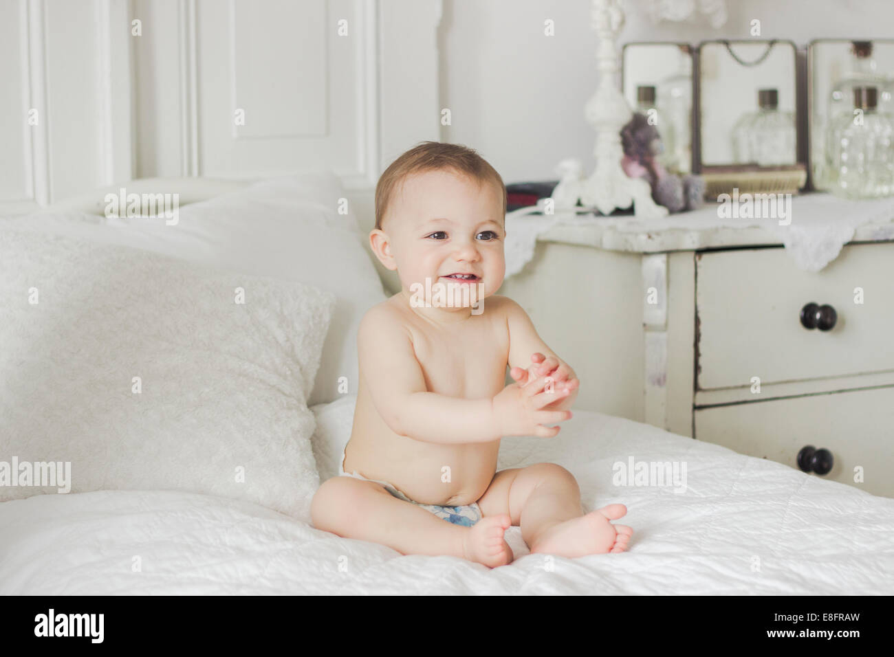 Portrait of Smiling baby sitting on bed in bedroom Stock Photo