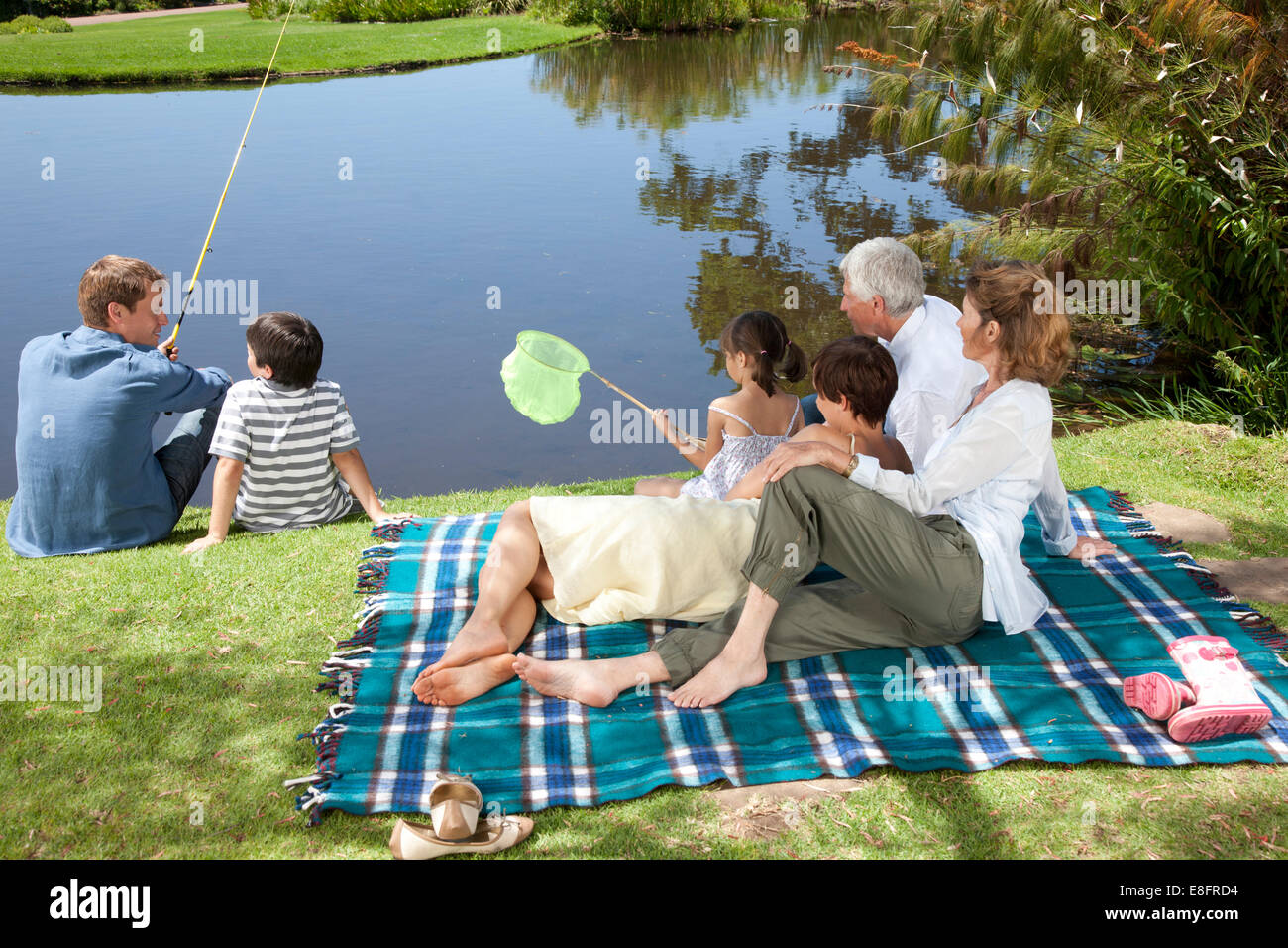 Multi-generation family sitting by lake fishing, Cape Town, Western Cape, South Africa Stock Photo