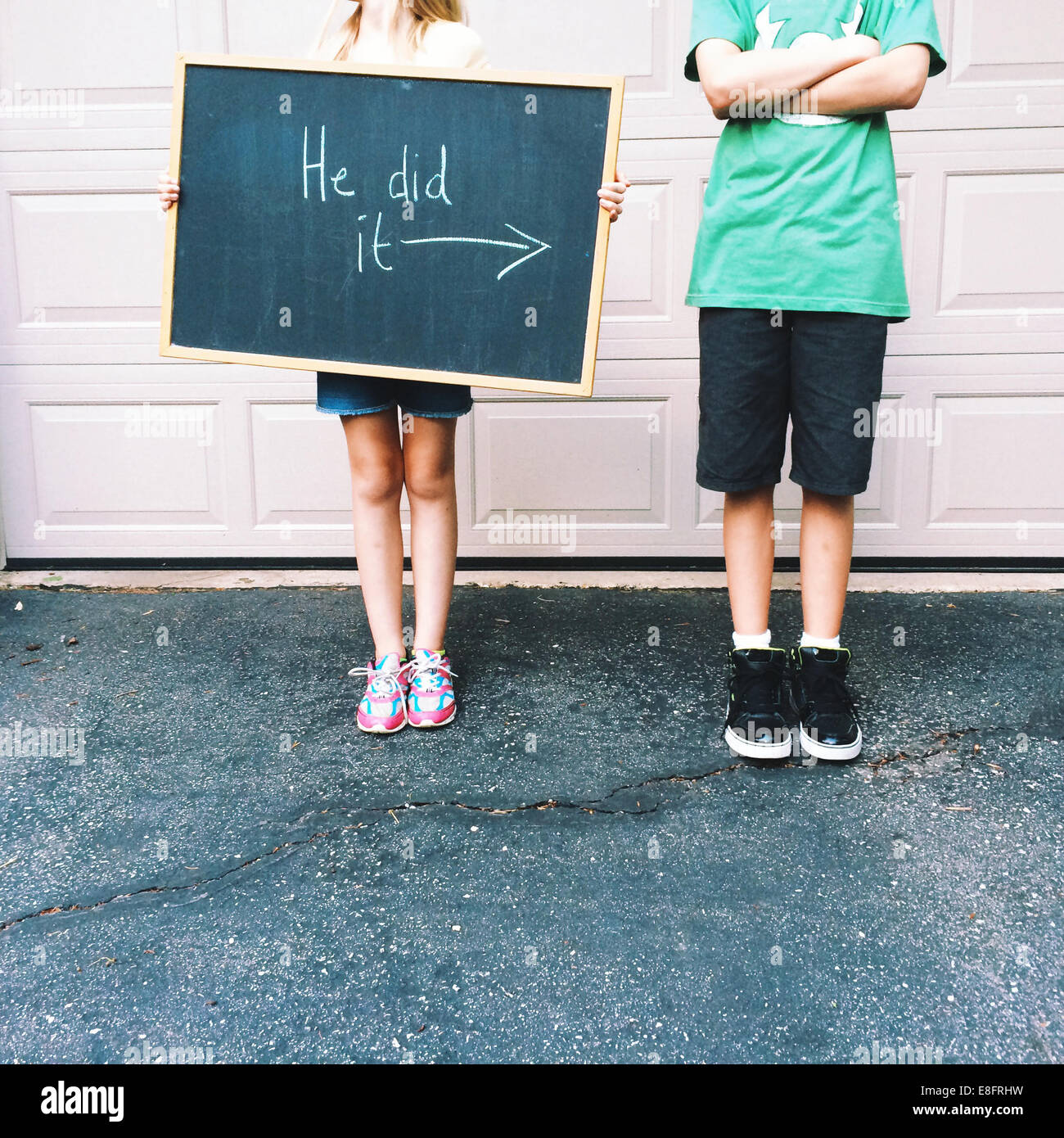 Boy standing next to a girl holding a blackboard saying he did it Stock Photo