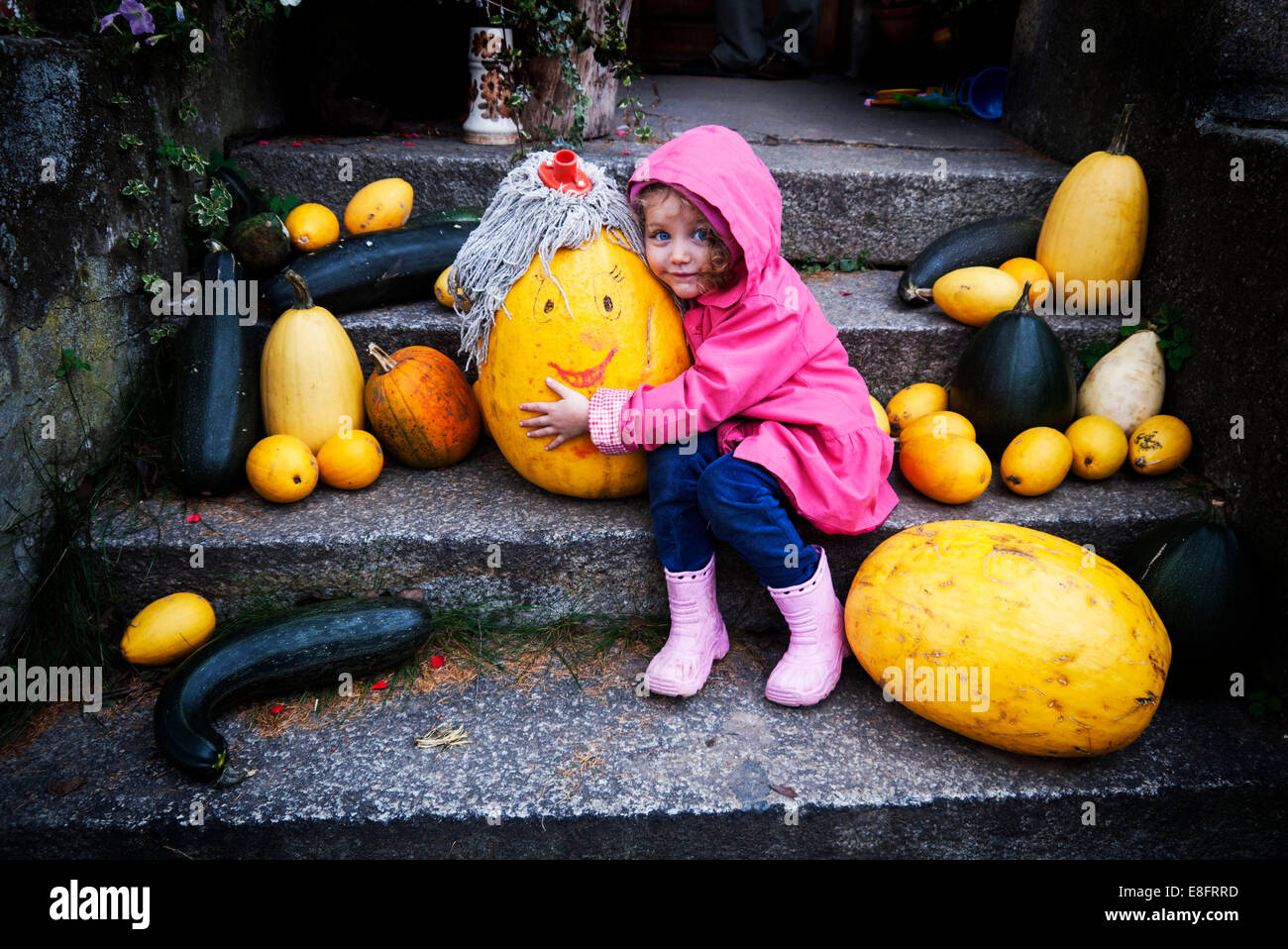 Girl sitting on steps hugging a pumpkin with a smiley face Stock Photo