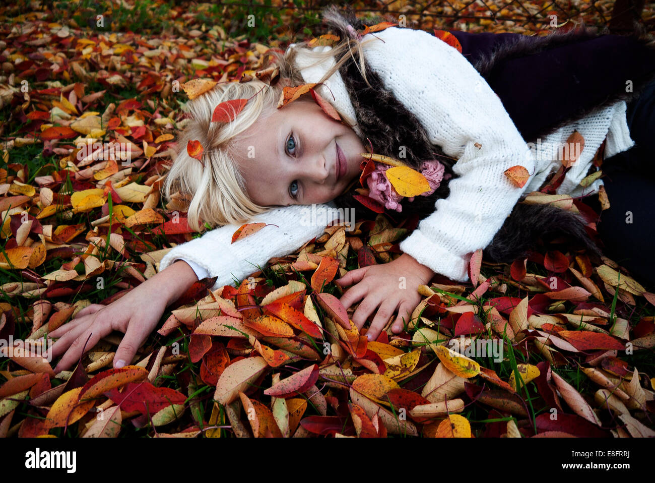 Smiling girl lying on grass amongst autumn leaves Stock Photo