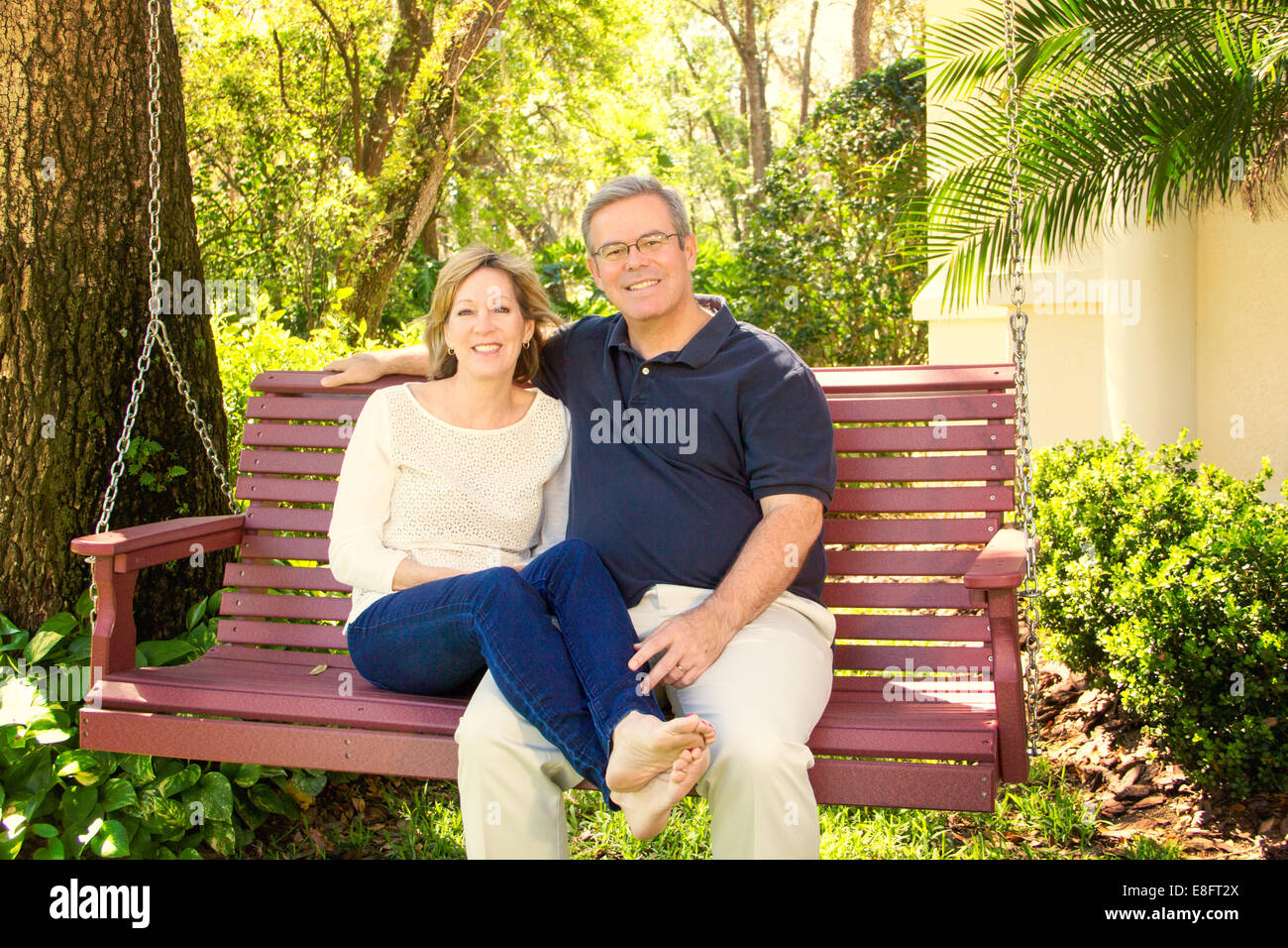 Mature couple sitting on wooden swing in garden Stock Photo