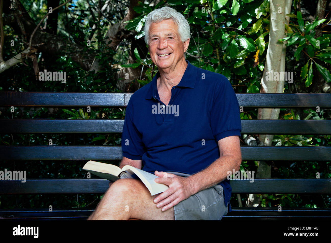 Senior man sitting on a bench reading a book in the garden Stock Photo ...