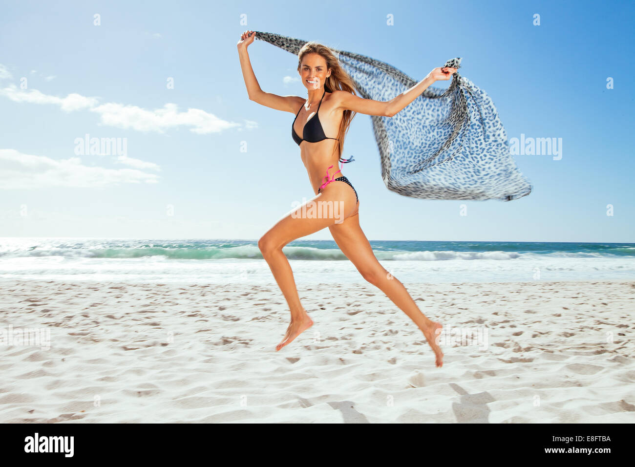 Young woman running along beach holding a scarf, Cape Town, Western