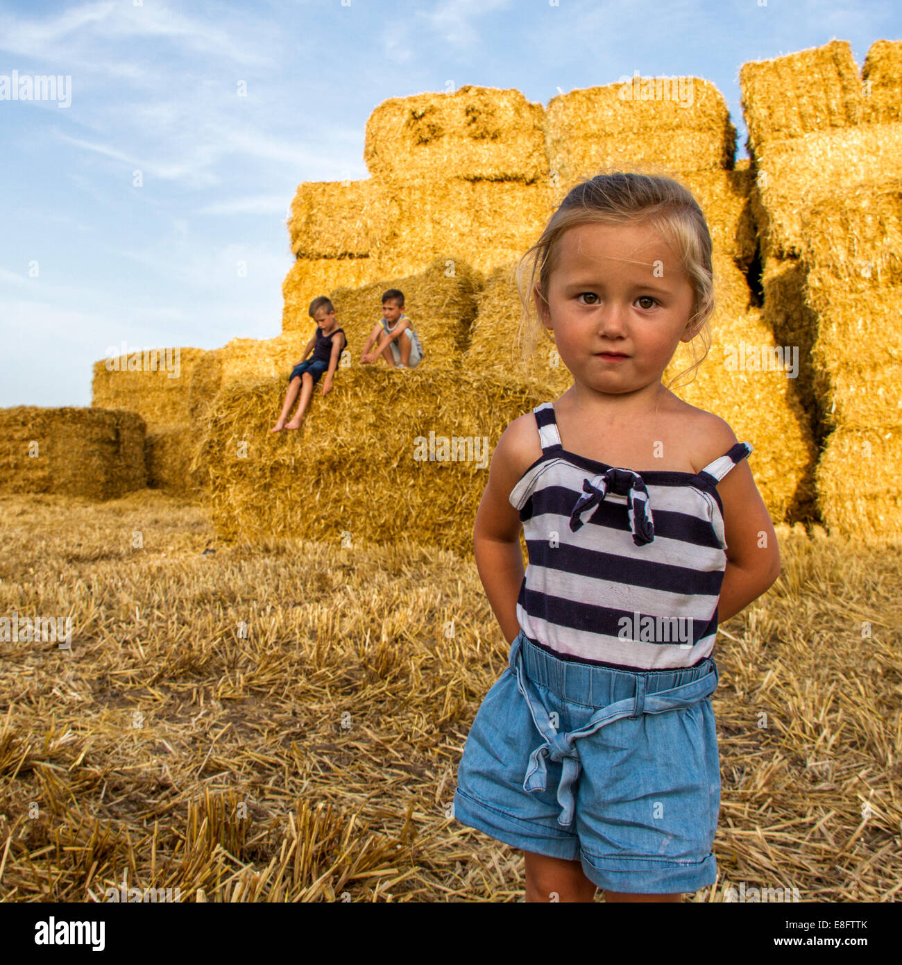 Three children playing in a field of hay bales, England, UK Stock Photo