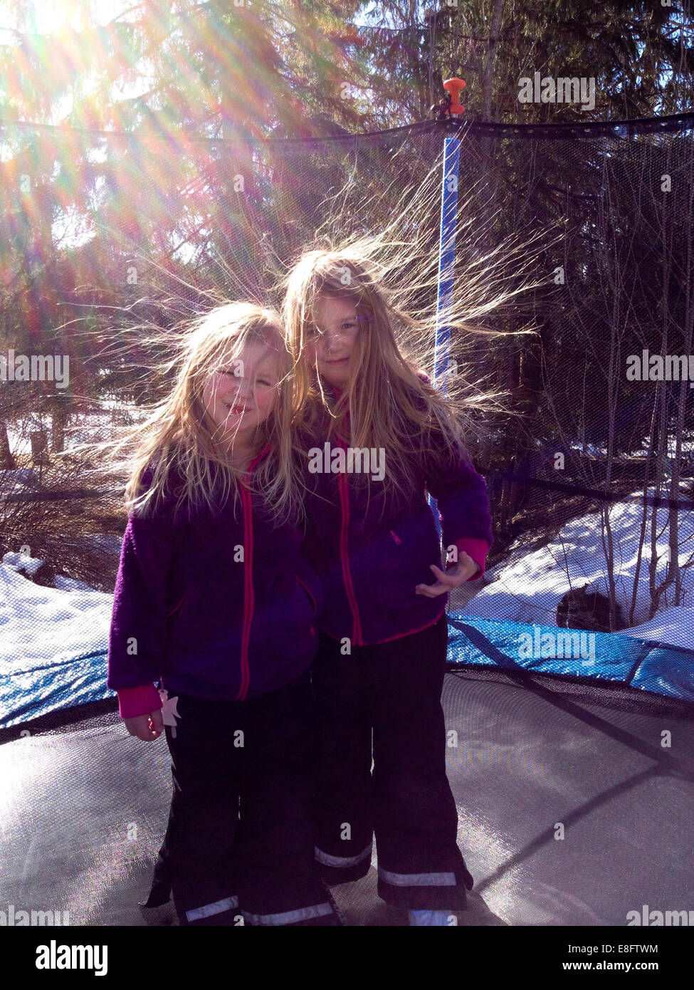 Two girls with static hair standing on a trampoline in the garden, Sweden Stock Photo