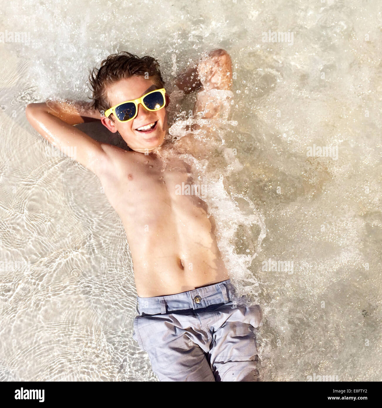 Overhead view of smiling boy lying in shallow sea with hands behind head Stock Photo