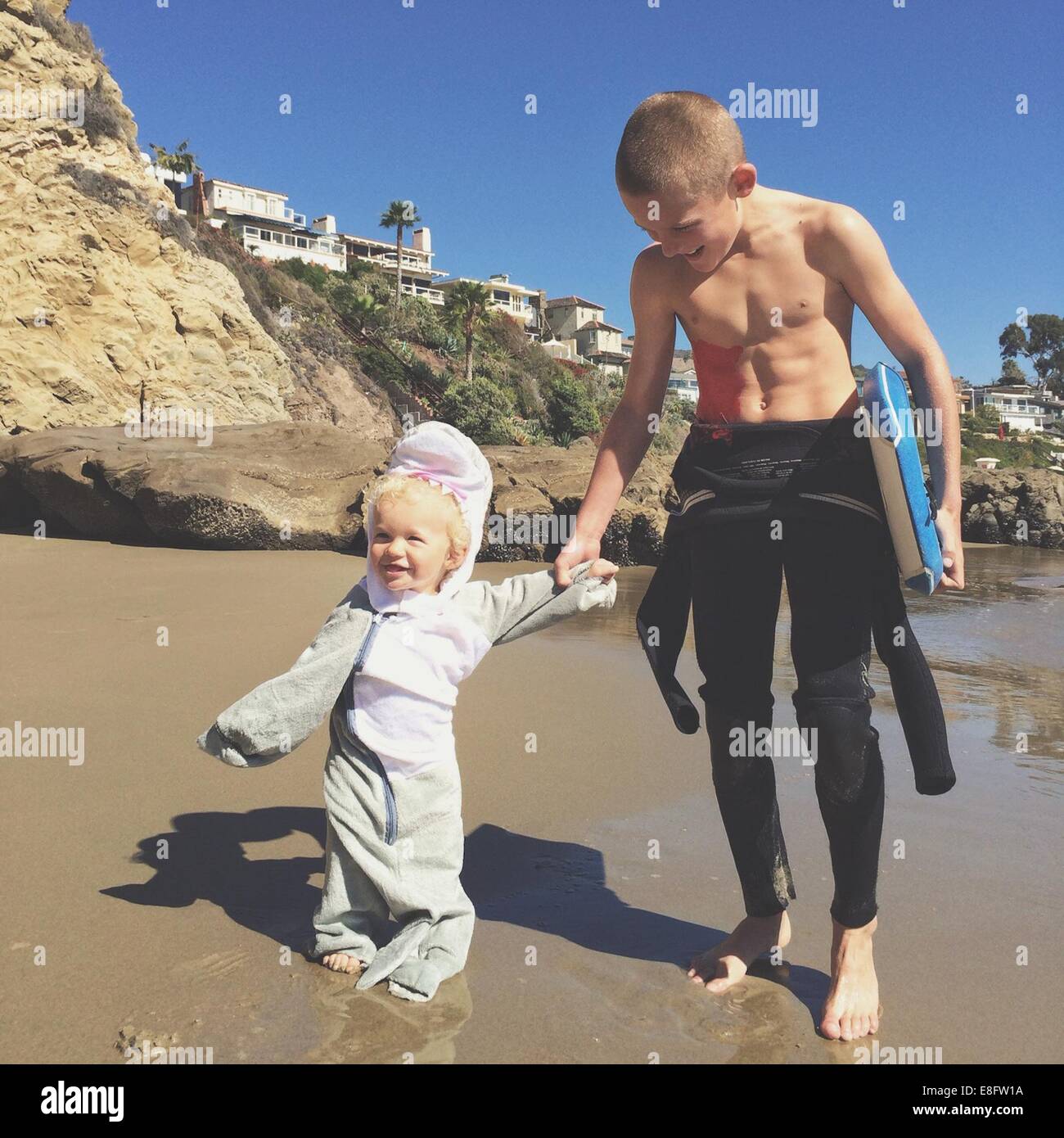 Two brothers holding hands on the beach with a surfboard Stock Photo