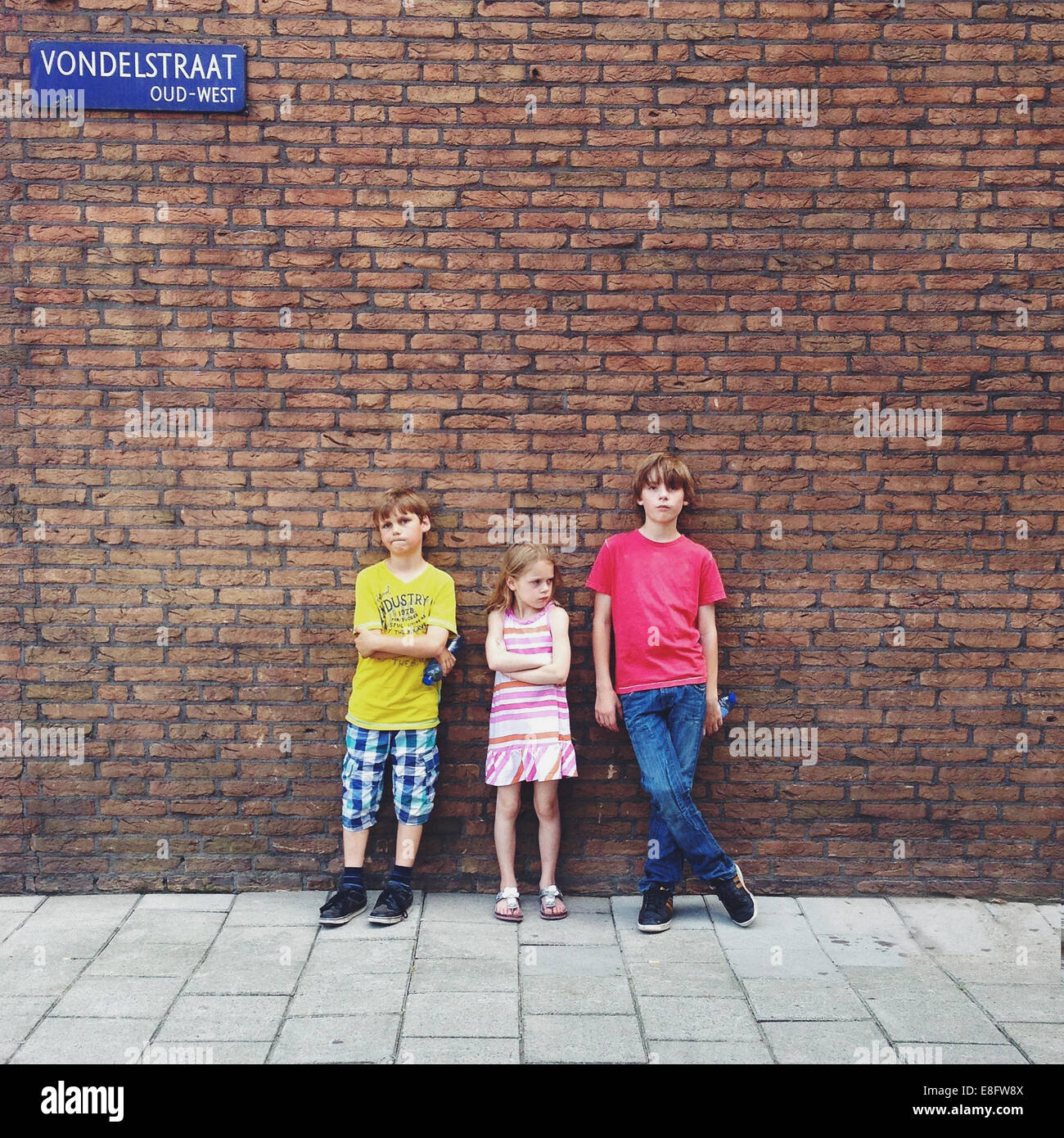 Three children standing in front of brick wall Stock Photo