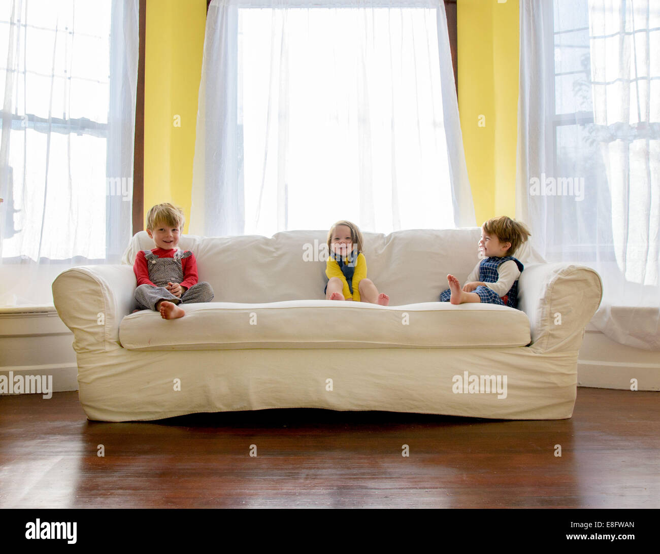 Three children sitting on a sofa in the living room Stock Photo