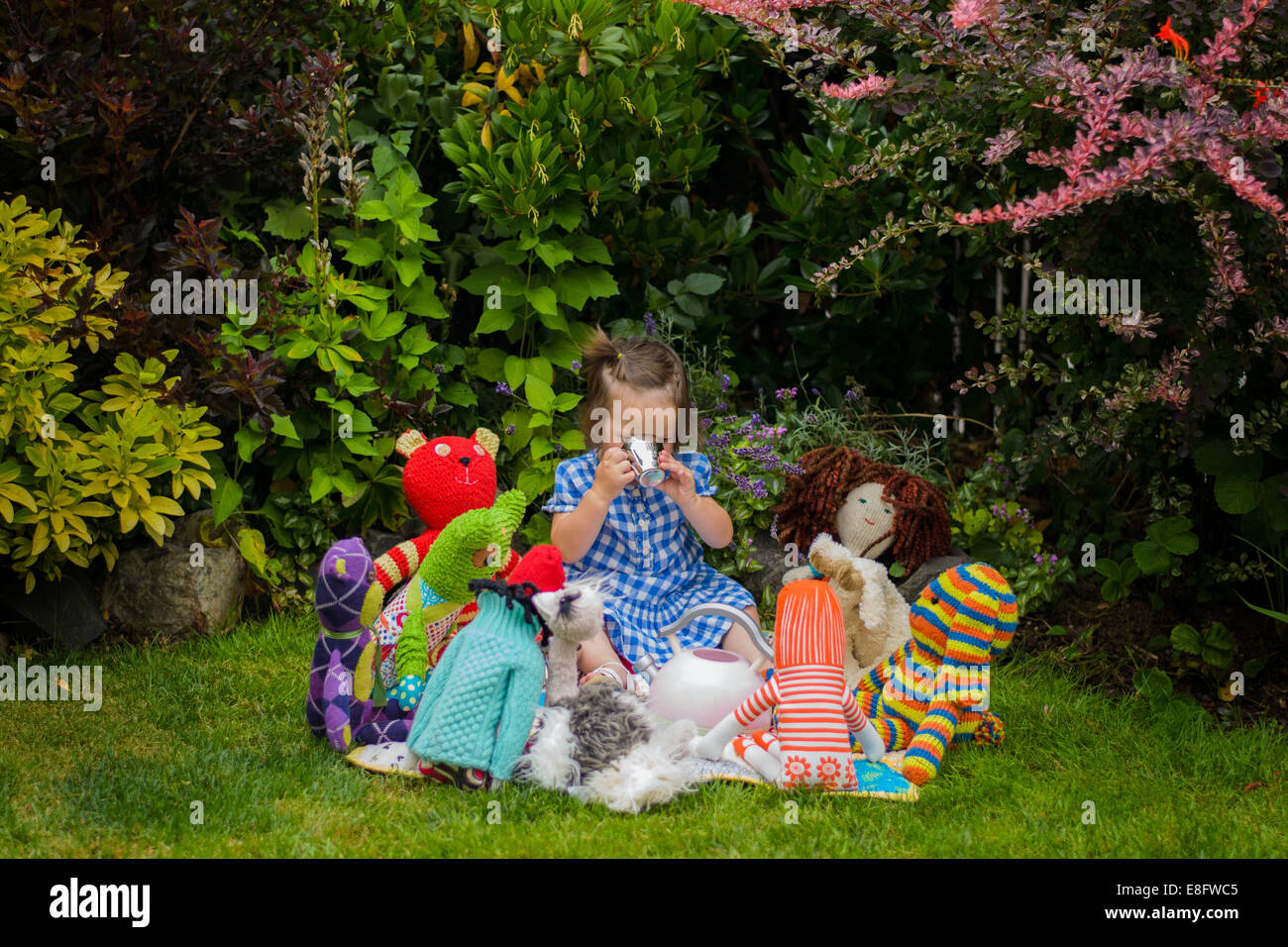 Girl sitting in the garden having tea party with her toys Stock Photo