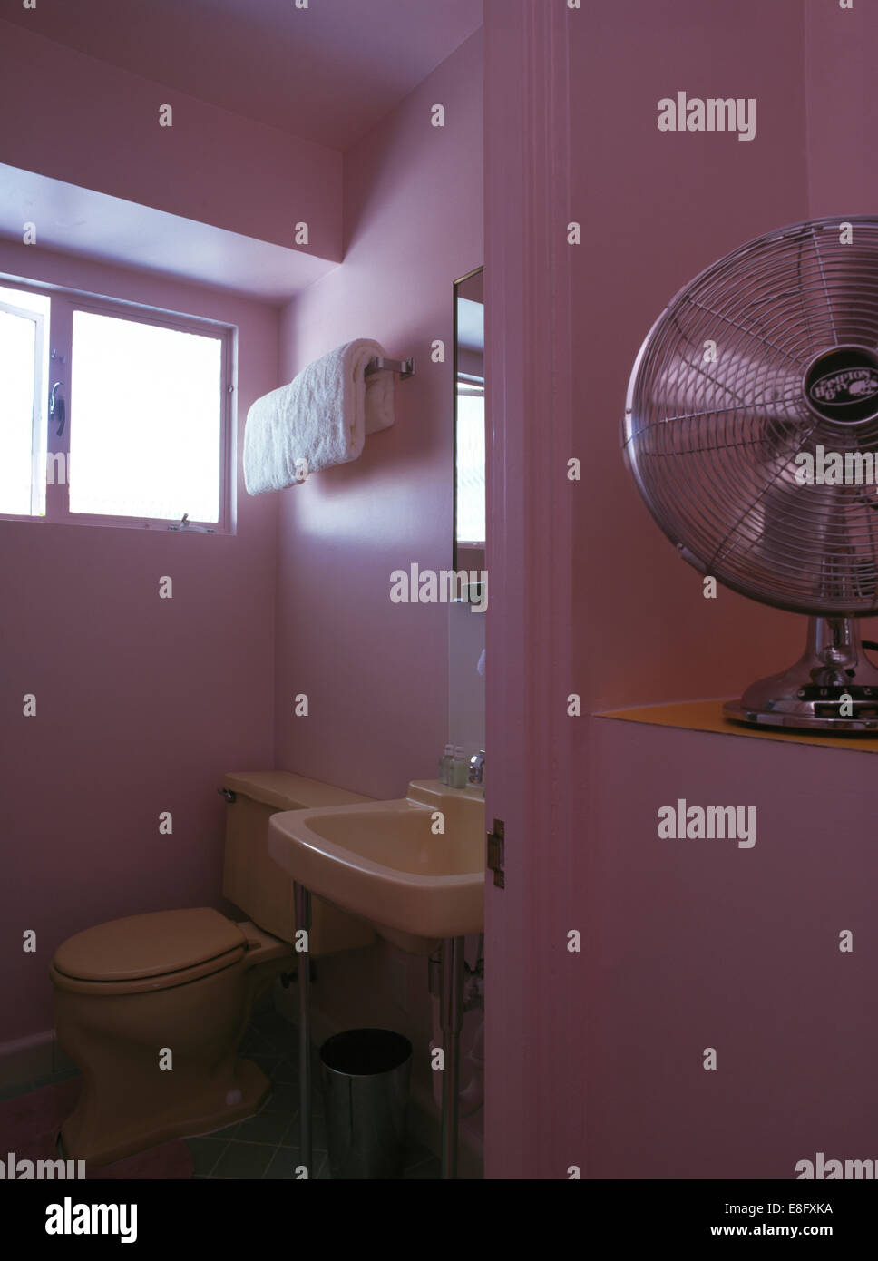 Freestanding electric fan on shelf in pink fifties style bathroom Stock Photo