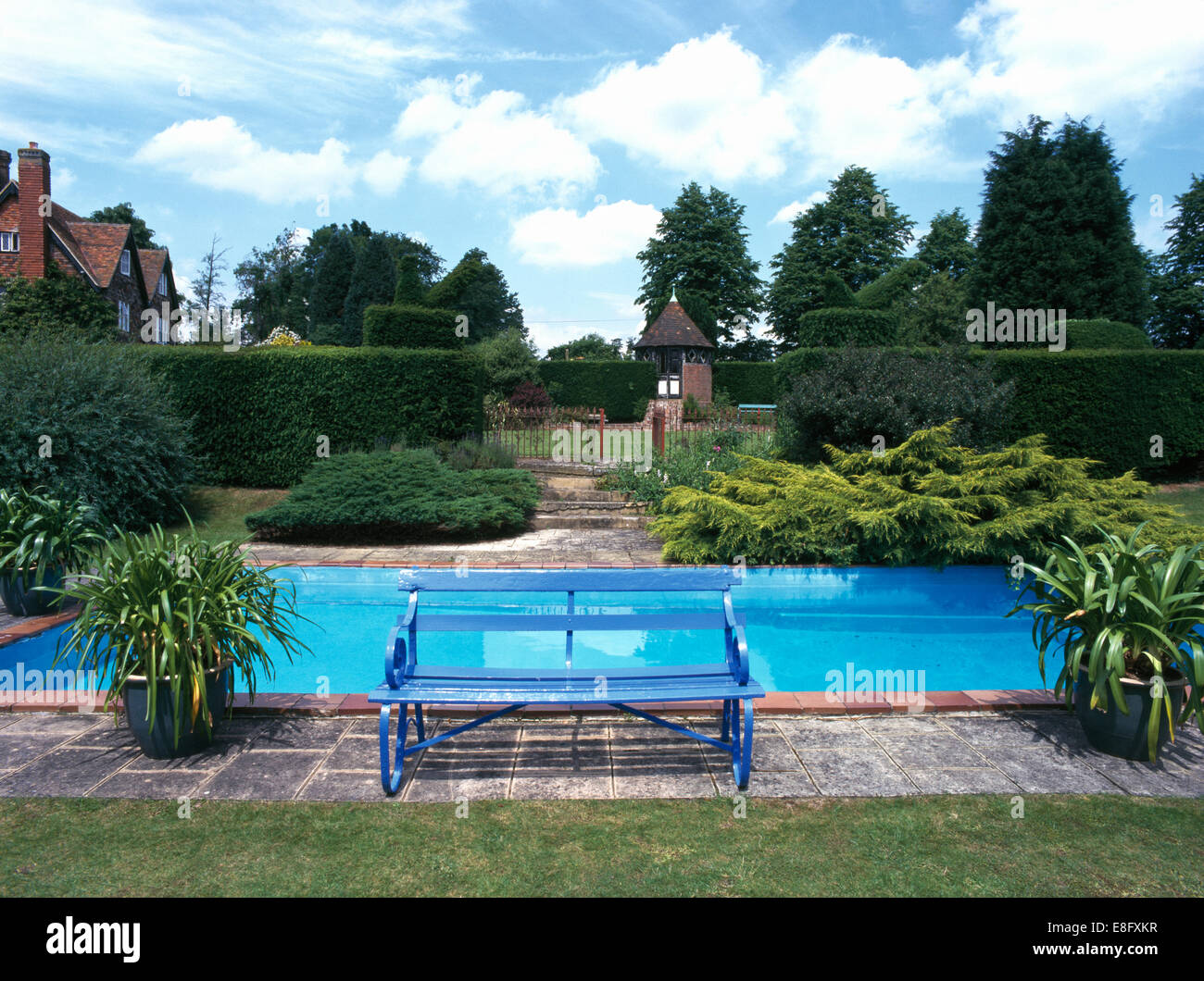 Blue painted bench on paving beside turquoise swimming pool in grounds of large country house Stock Photo