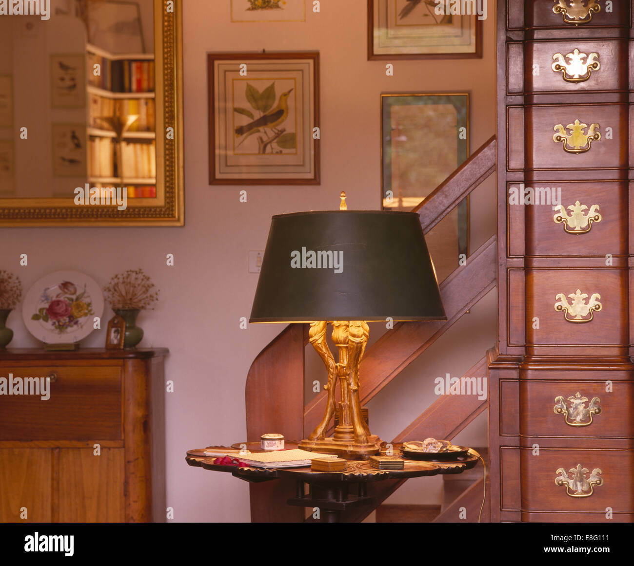 Lighted lamp on small table beside antique chest of drawers in traditional hall Stock Photo