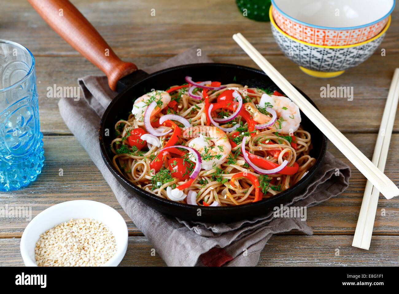Buckwheat noodles with shrimp, peppers and tomatoes in a frying pan