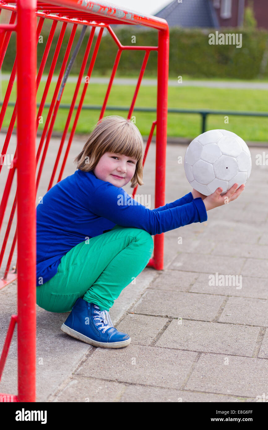 Young crouching girl with ball on hands in metal goal Stock Photo