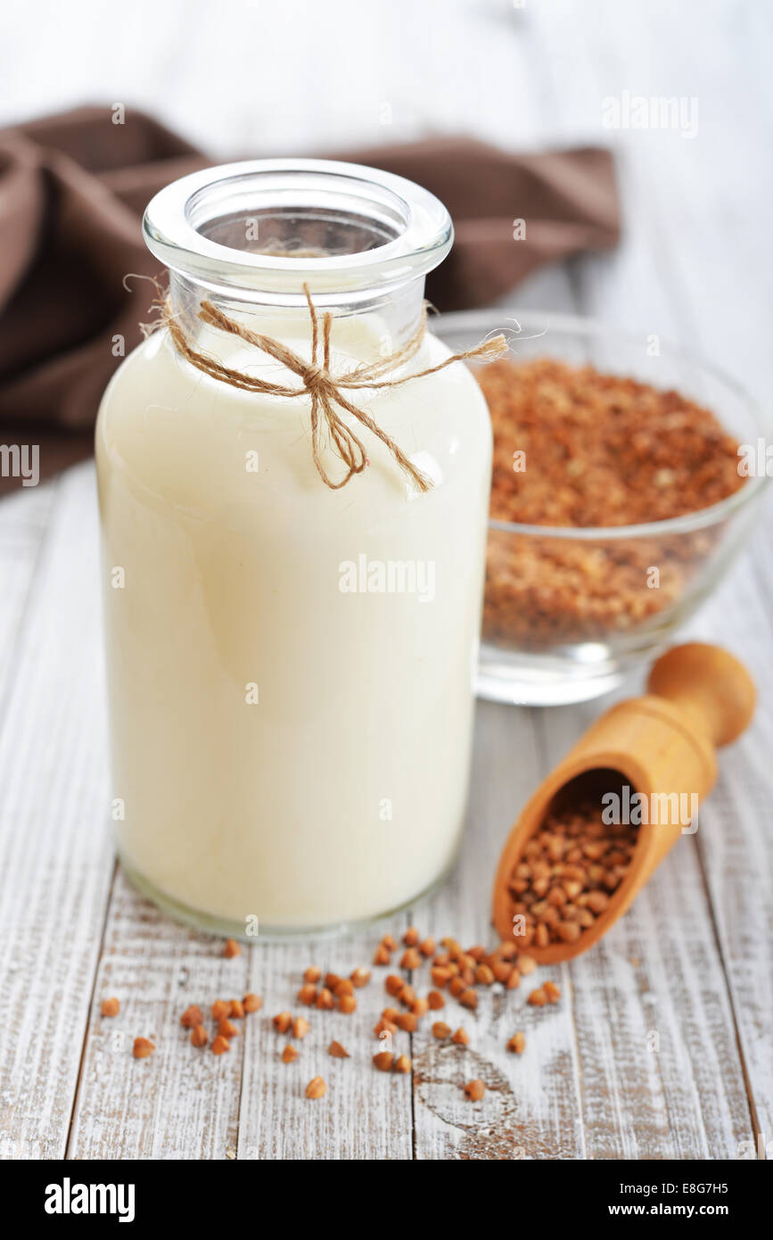 Buckwheat milk in bottle with dry buckwheat seeds on white wooden