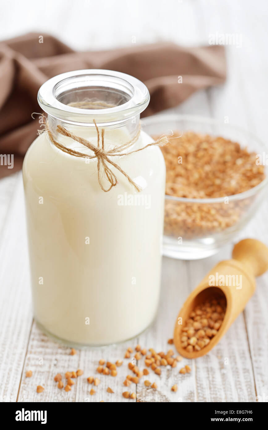 Buckwheat milk in bottle with dry buckwheat seeds on white wooden