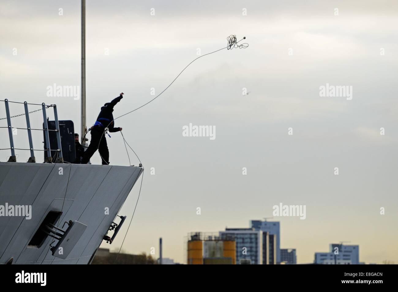 A crewman of HMS Defender throws out a line to tie up as the ship docks