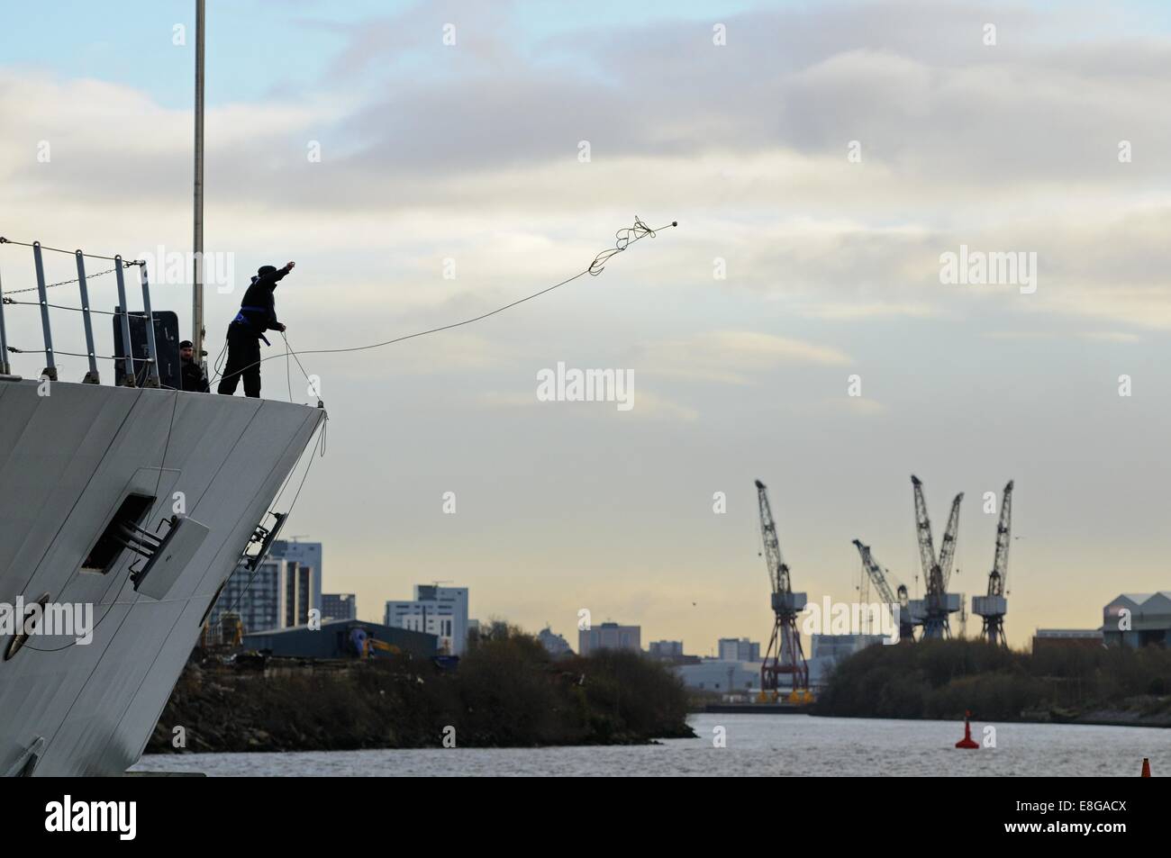 A crewman of HMS Defender throws out a line to tie up as the ship docks