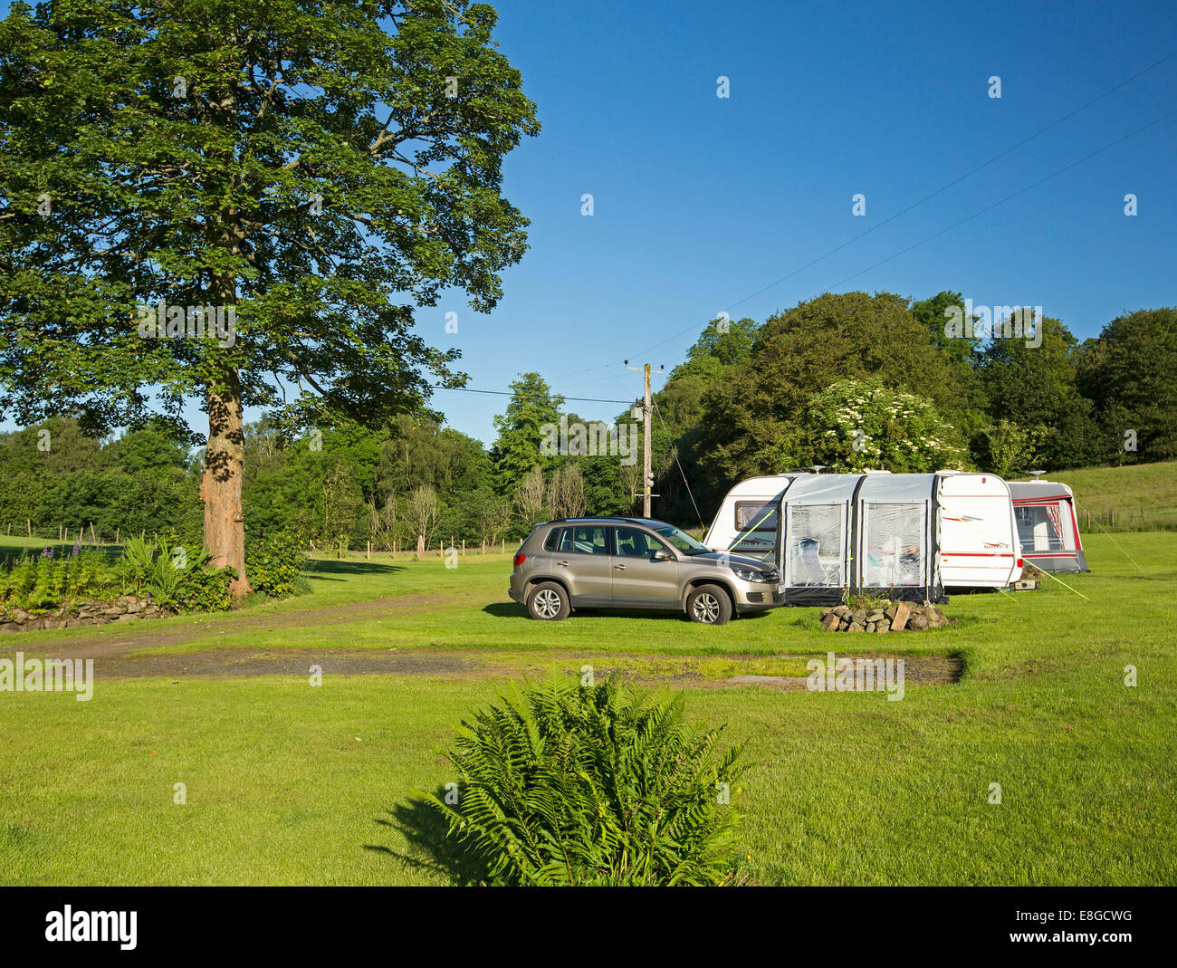 Inexpensive camping site with caravan with annexe set up beside car / SUV in field with lawns & shading trees on English farm Stock Photo