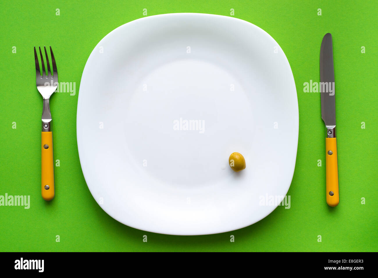 white plate with one olive and cutlery on green tablecloth Stock Photo
