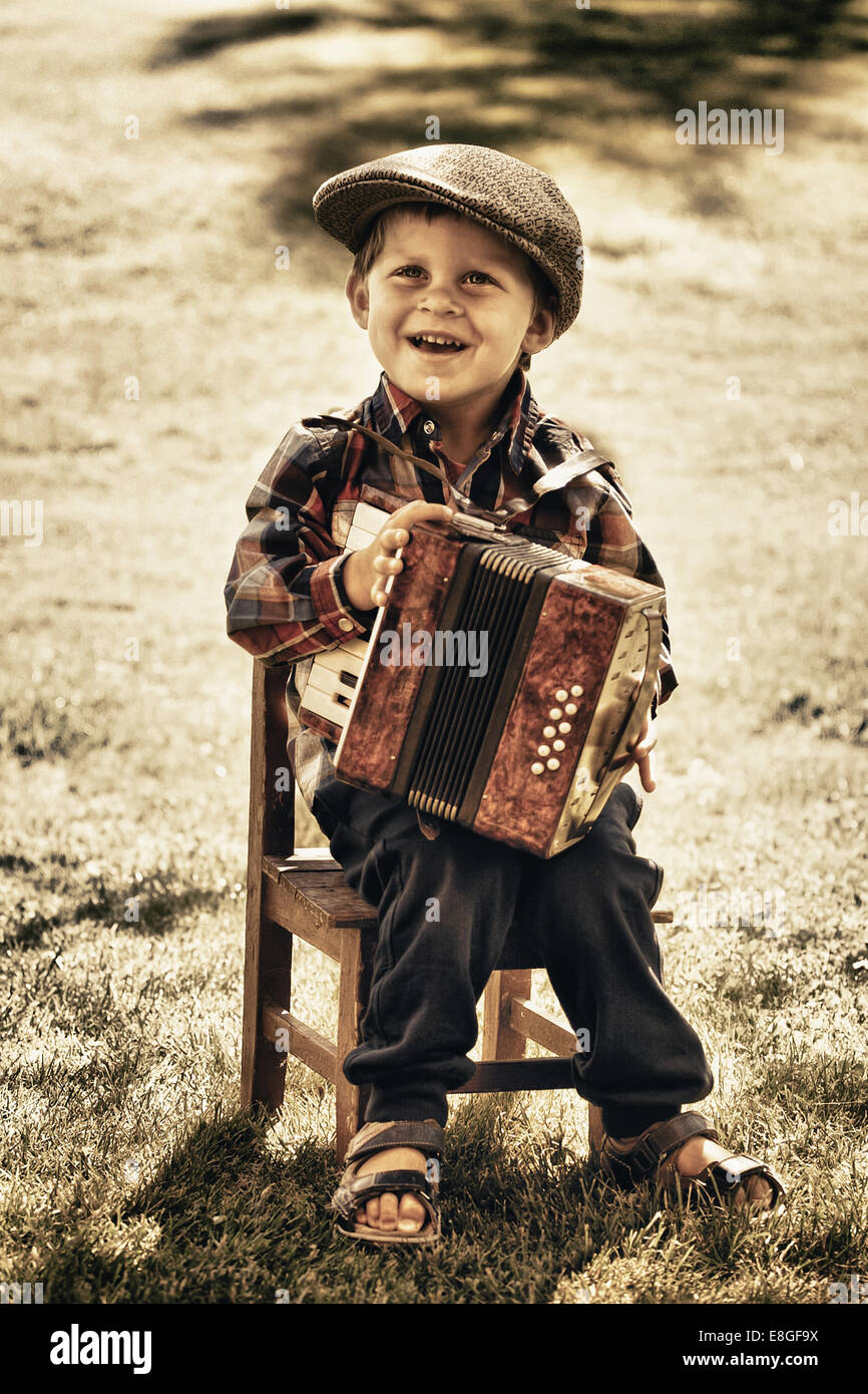 happy young boy wears retro or vintage style playing accordion outdoor