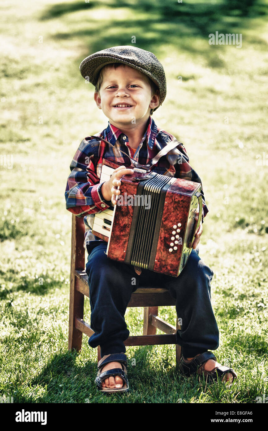 happy young boy wears retro or vintage style playing accordion outdoor in garden on summer Stock Photo