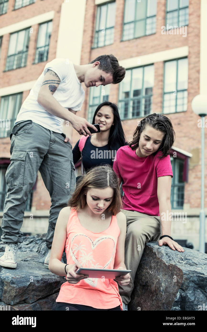 High school students using technologies on rock at schoolyard Stock ...