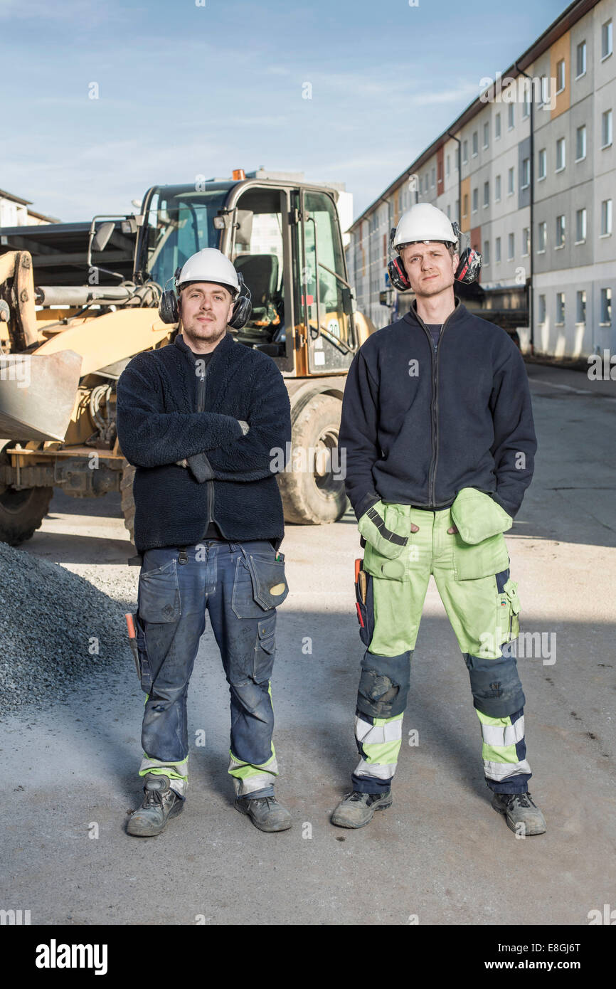 Full length portrait of confident workers standing at construction site ...