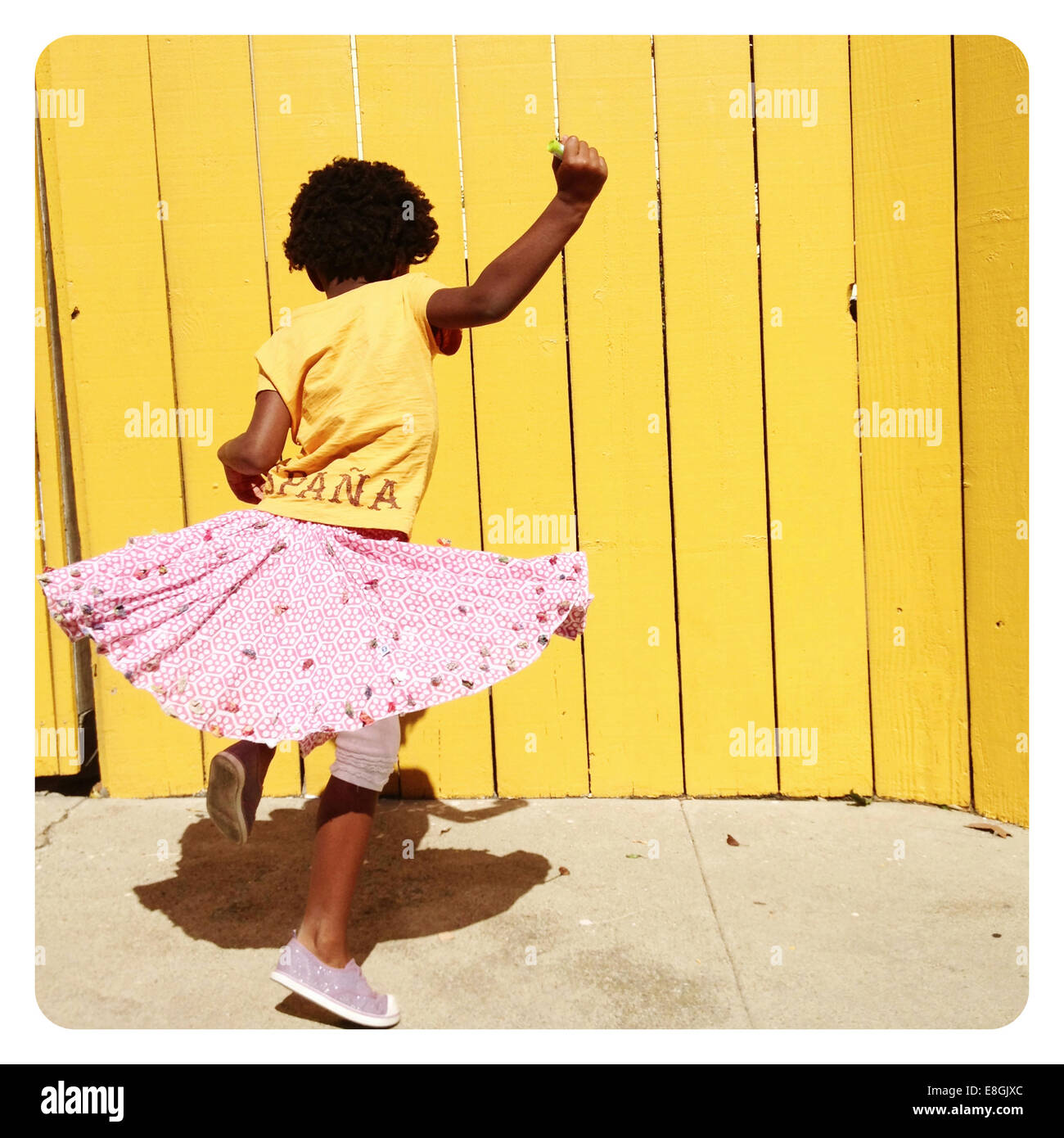 Girl spinning around dancing in front of a yellow wall, San Francisco, California, USA Stock Photo