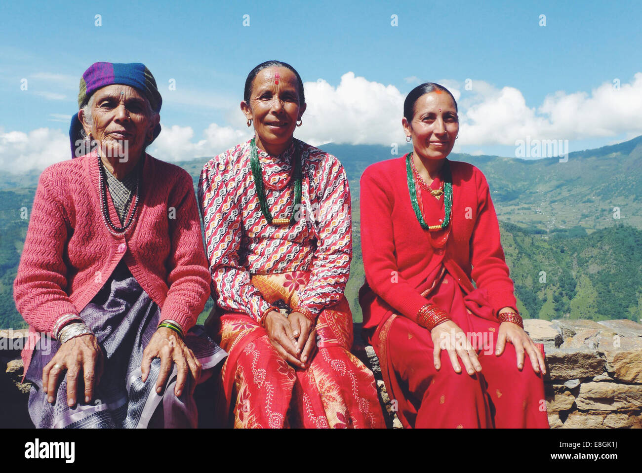 Portrait of three local Nepalese women sitting on a wall in a mountain village, Nepal Stock Photo