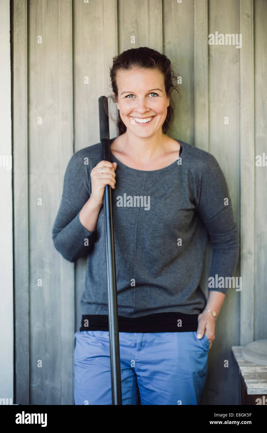 Portrait of happy woman holding shovel while standing against wall Stock Photo