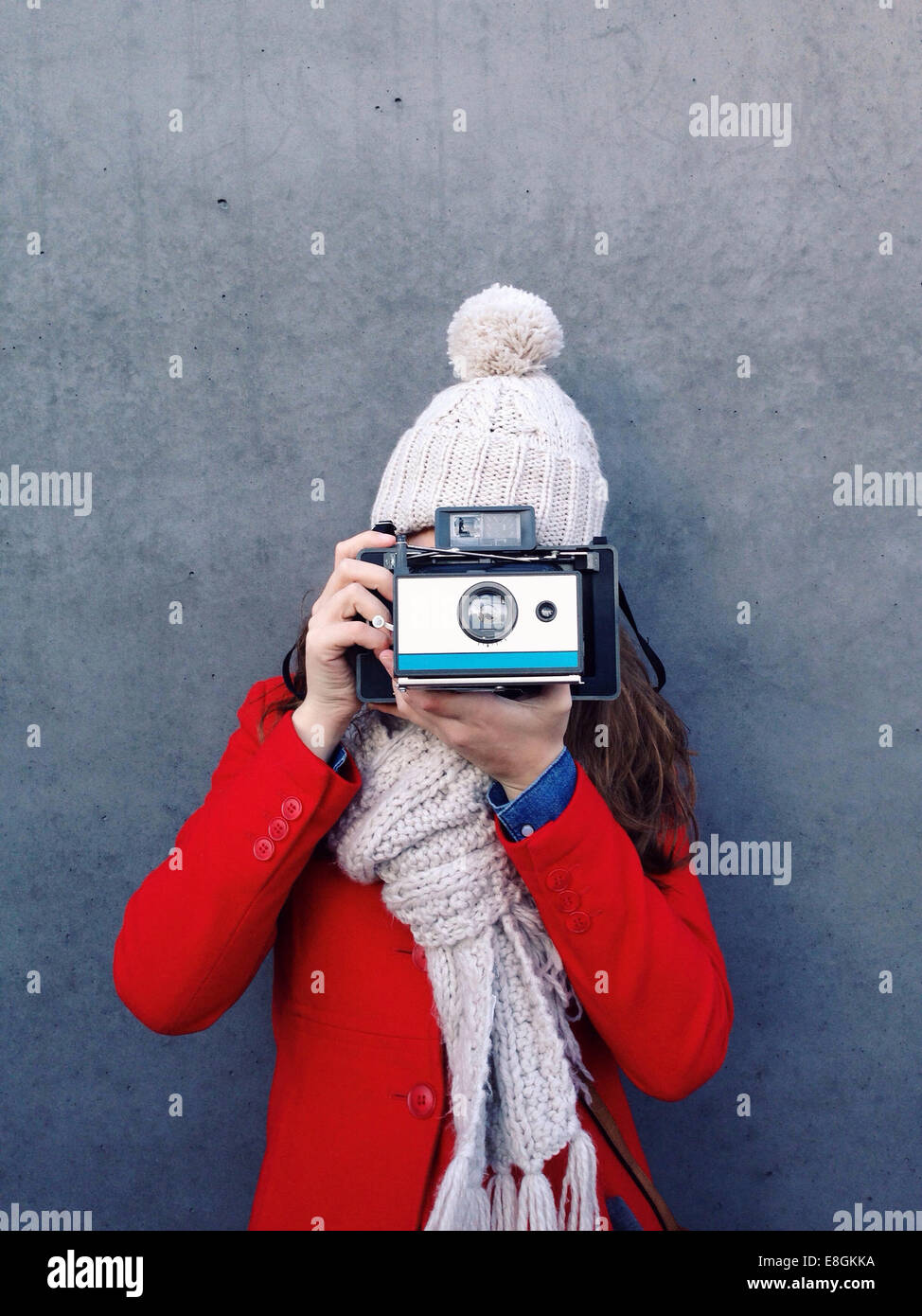 Young woman standing in front of a wall taking a photograph with an instant camera Stock Photo