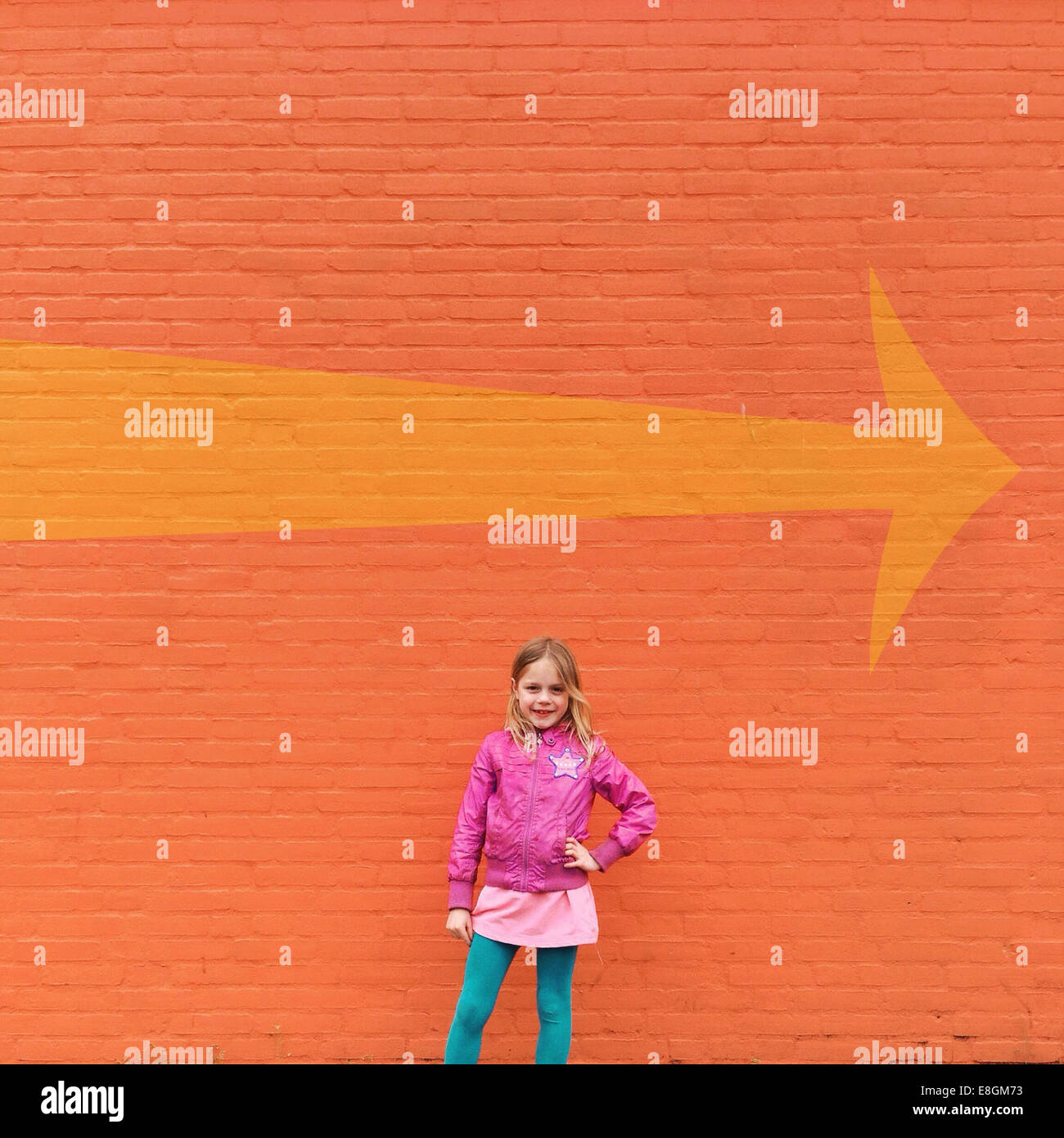 Girl standing in front of orange wall and a directional arrow Stock Photo