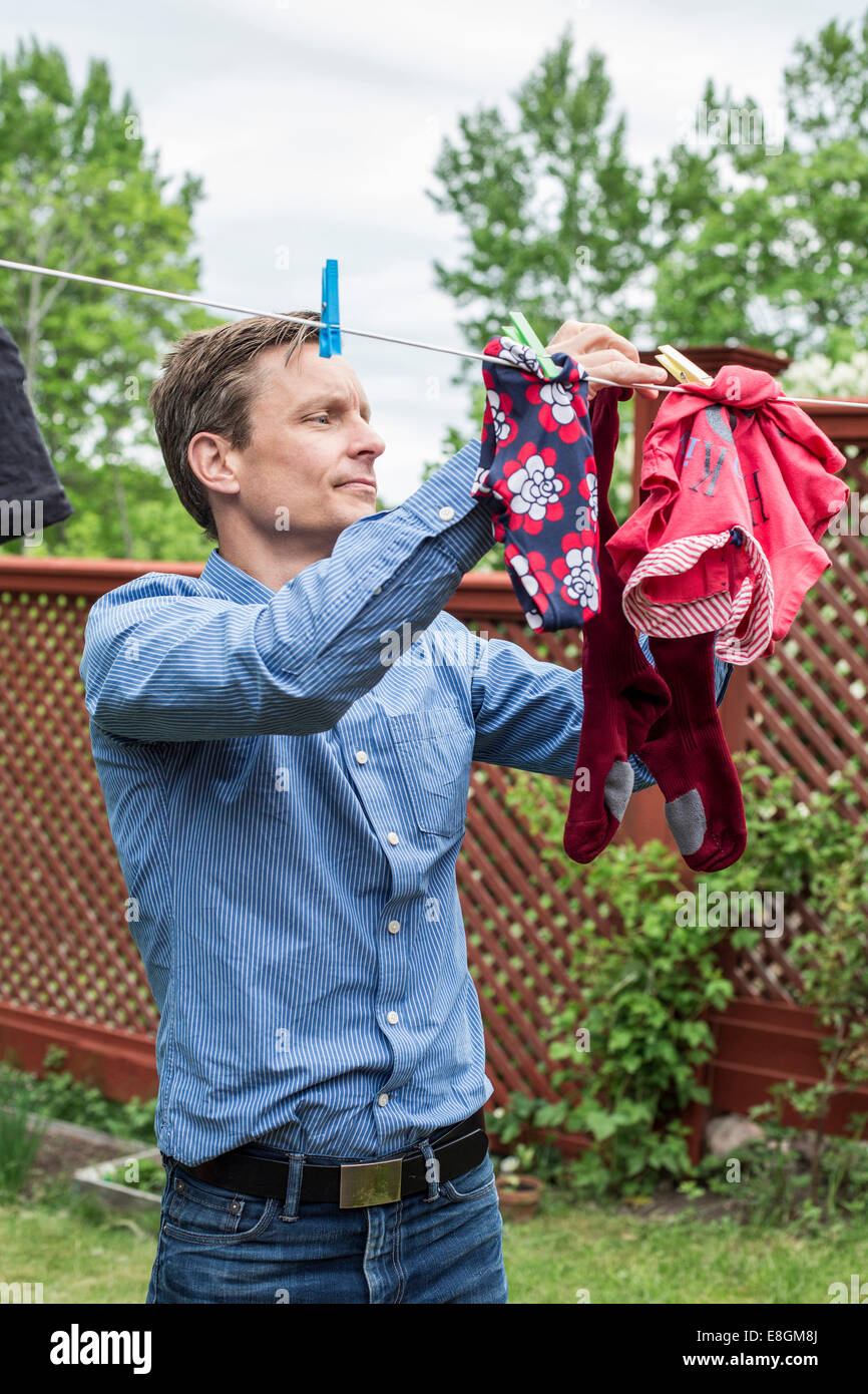 Mid adult man removing clothes from clothesline at yard Stock Photo