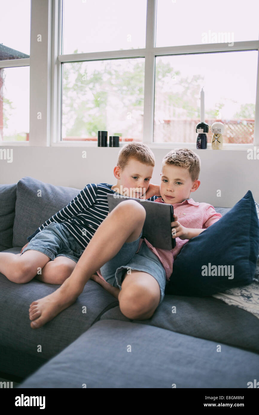 Siblings using digital tablet on sofa at home Stock Photo - Alamy