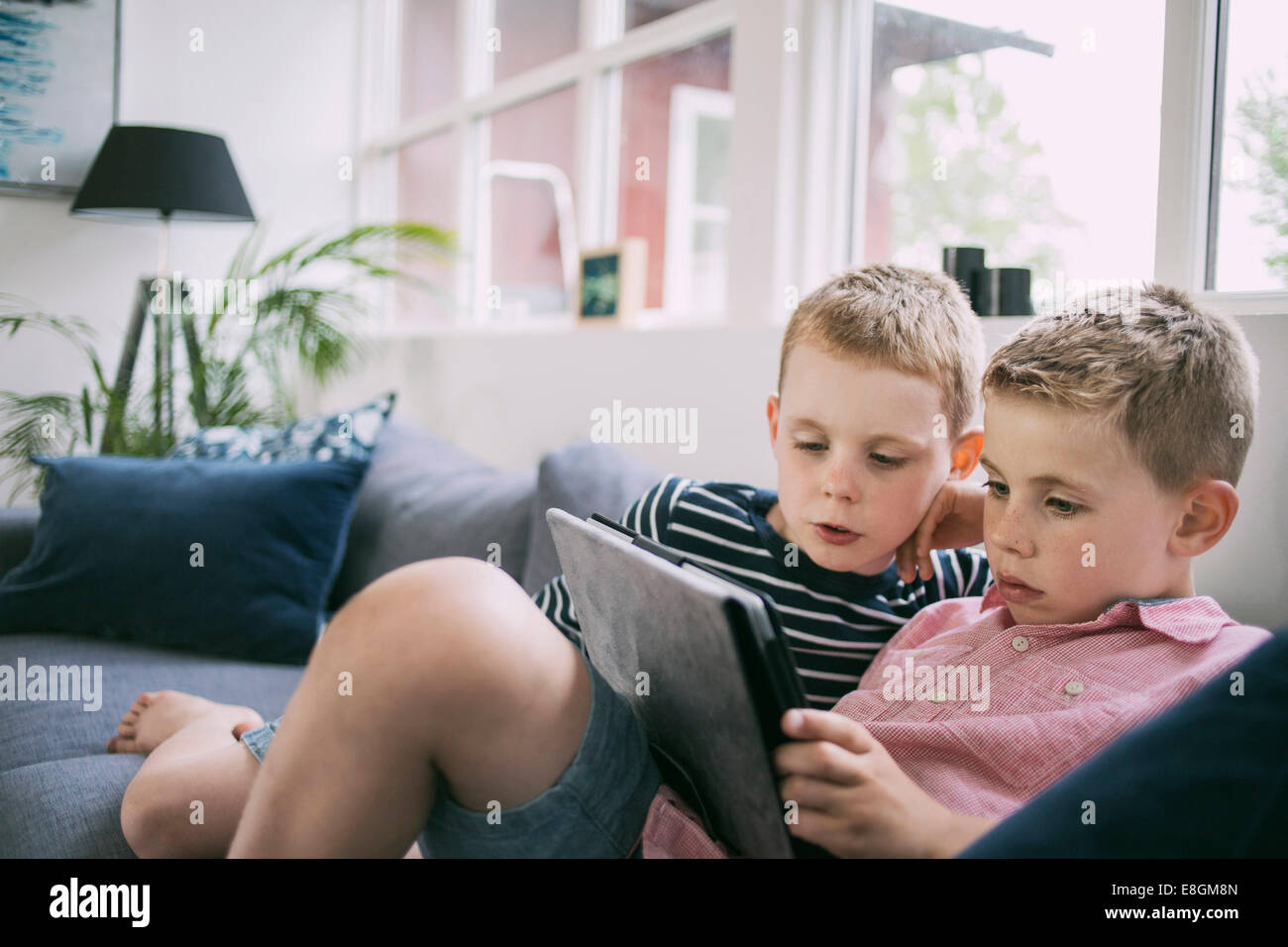 Brothers using digital tablet on sofa at home Stock Photo
